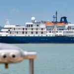 The expedition cruise ship Caledonian Sky anchored in calm waters, showing its blue hull and white superstructure